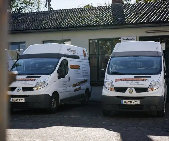 Zwei weiße Firmenfahrzeuge mit Beschriftung stehen vor einem Gebäude mit Tauschfenster.