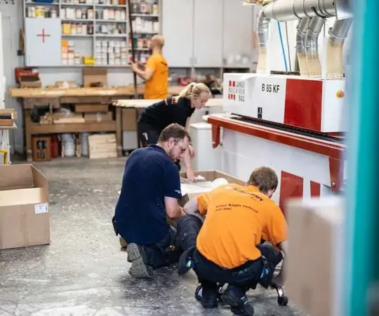 Mehrere Personen arbeiten in einer modernen Tischlerei mit Maschinen und Werkbänken.