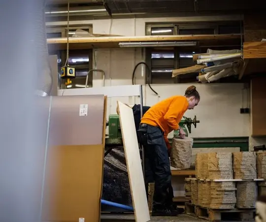 Handwerkerin stapelt Holzplatten in einer modernen Werkstatt für Holzverarbeitung und Handwerk.