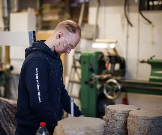 Handwerker mit Schutzbrille arbeitet in einer modernen Holzwerkstatt an Holzplatten.