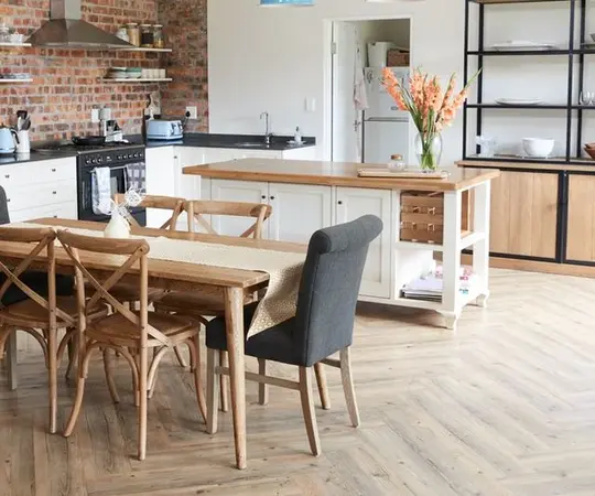 Moderne Landhausküche mit Holztisch, Kücheninsel, offenen Regalen und Backsteinwand.