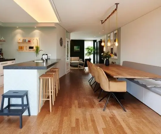 Moderne offene Wohnküche mit Holzboden, Kücheninsel, Essbereich und stilvoller Beleuchtung.